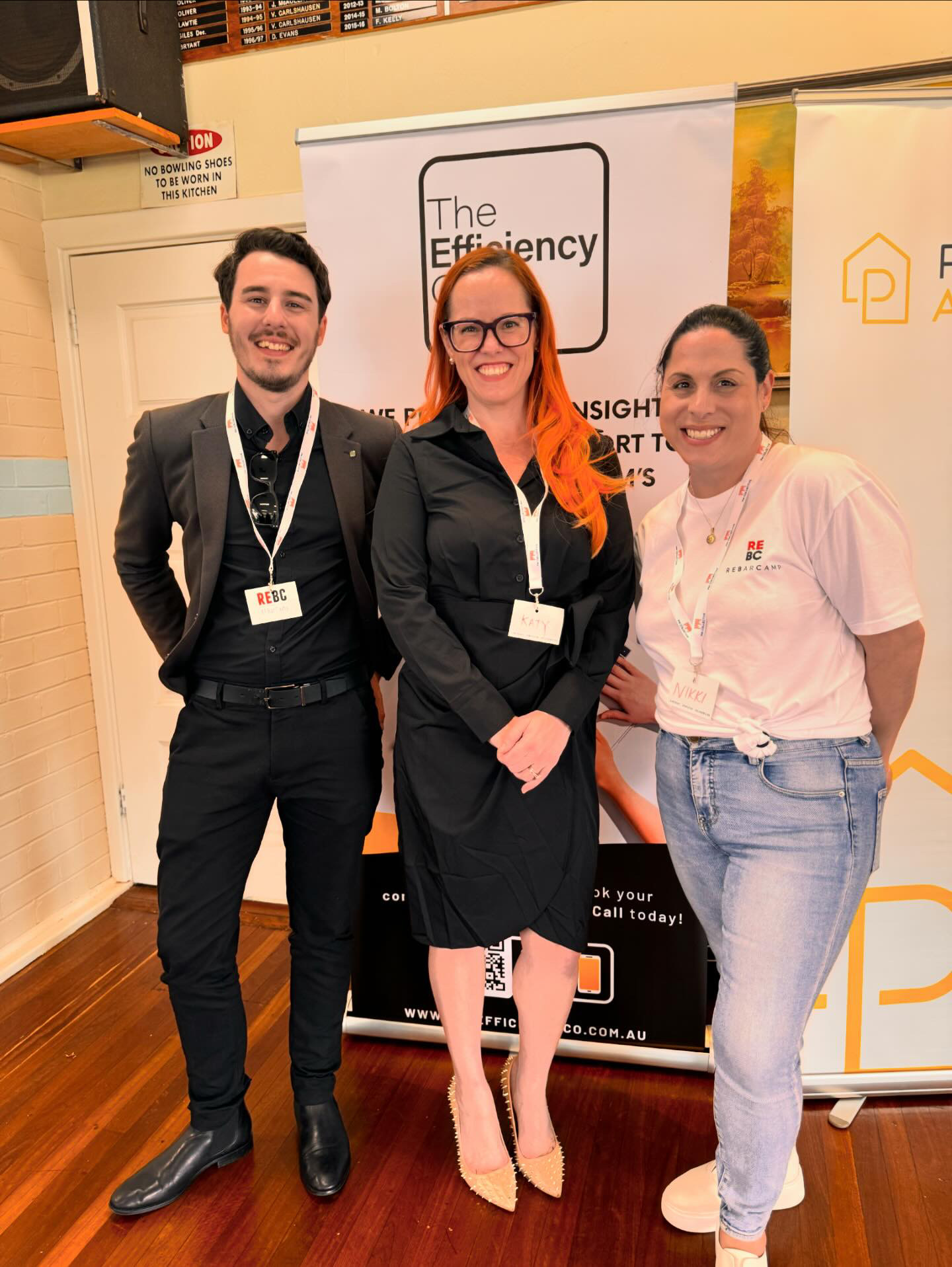a picture of Joe Shannon, Katy ONeill and Nikki D'Agostino standing infront of an Efficiency Co pull up banner at REBC event 2024